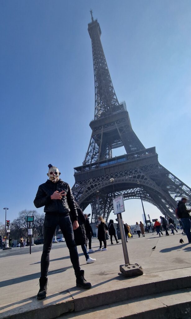 Un homme portant un masque pose devant la tour Eiffel, illustrant un moment unique dans la ville lumière.